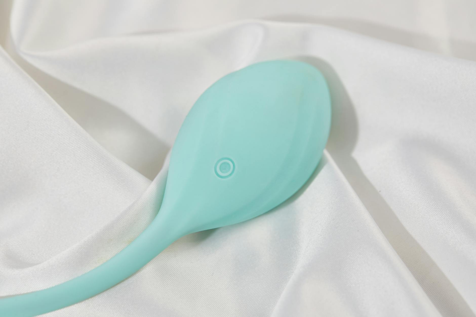 A stylish teal vibrator on smooth white silk fabric, symbolizing intentional pleasure despite medication side effects