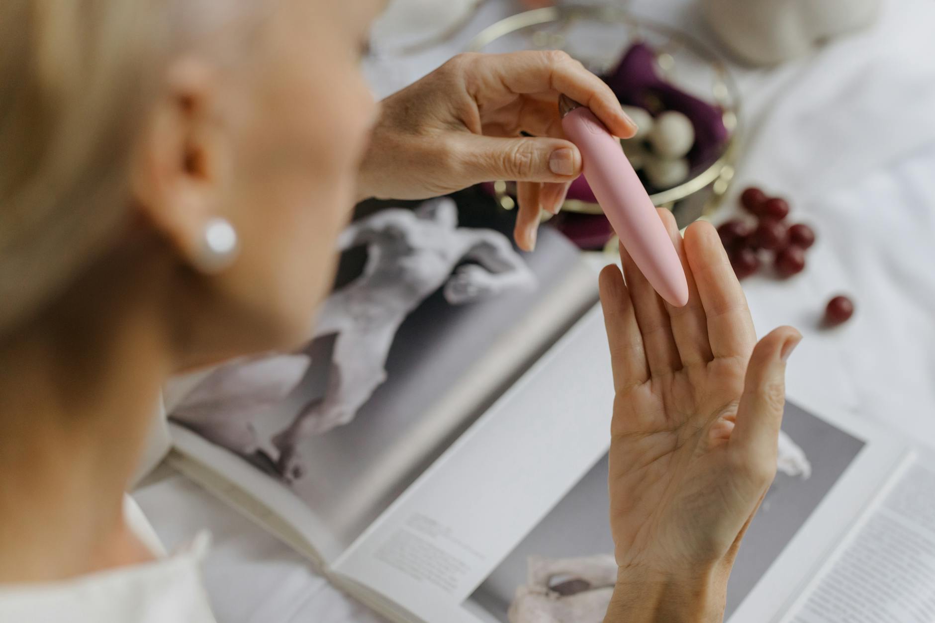 Woman with eyeglasses holding blue and pink silicone vibrators in a contemplative manner.