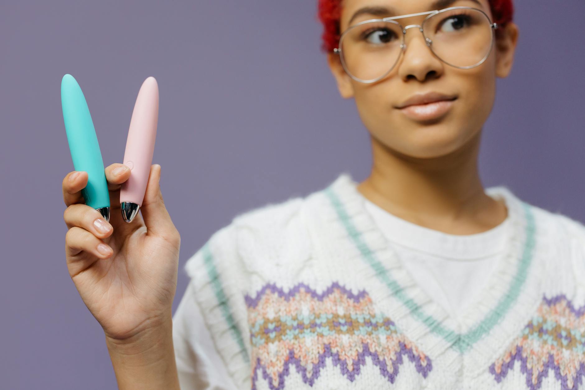 A woman holding colorful vibrators against a vibrant background, exploring modern pleasure tools.