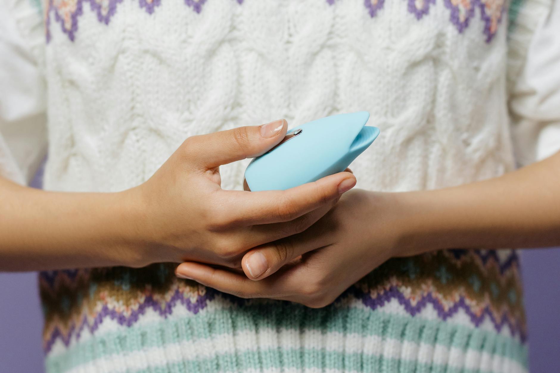 A blue silicone vibrator held in hand against a purple background, representing self-love and sexual wellness.