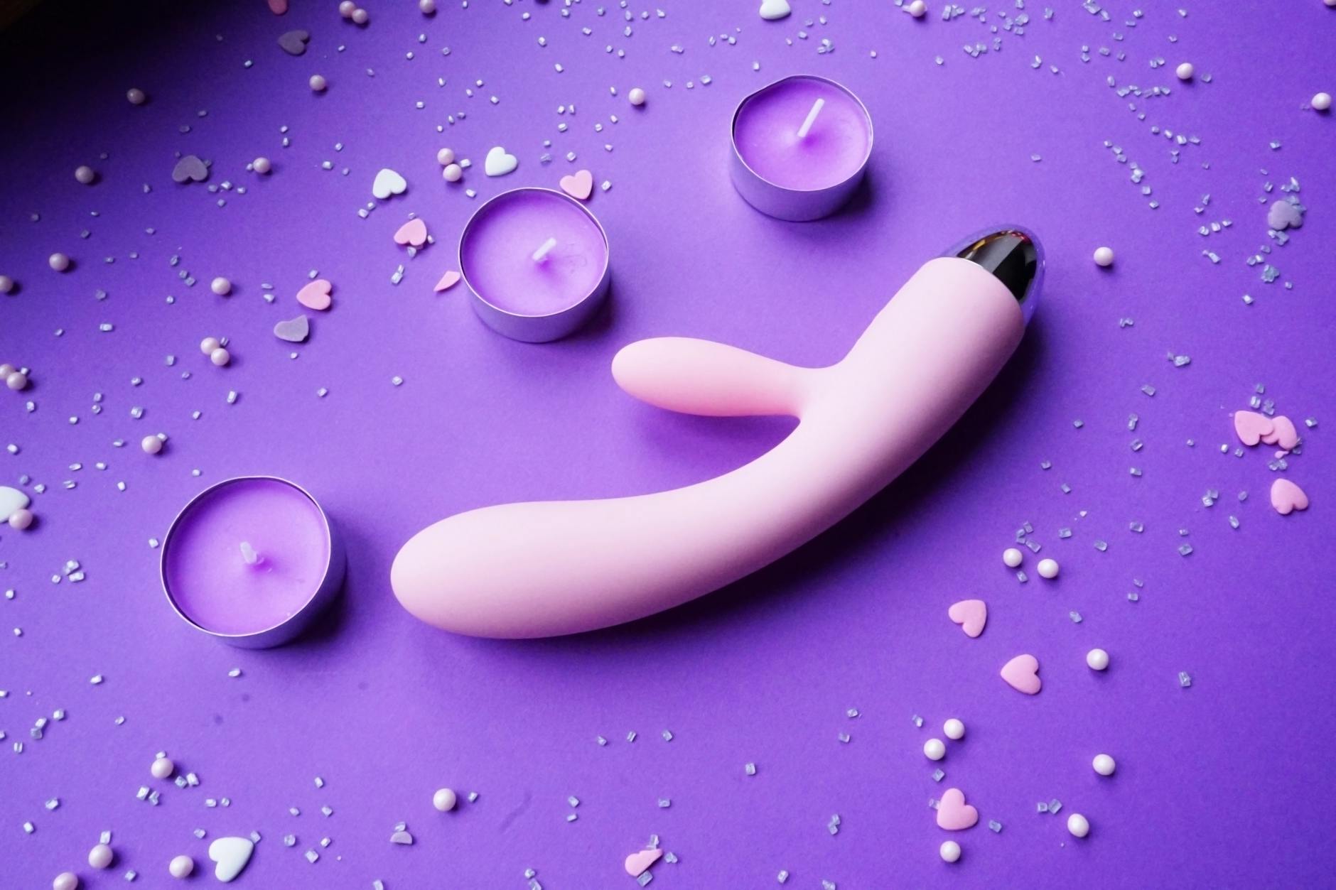 Pink vibrator surrounded by heart confetti and candles on purple background for long-distance intimacy
